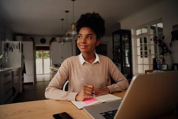 Succesvolle jonge ondernemer denken tijdens het schrijven in het dagboek en met behulp van laptop thuis met behulp van coronavirus lockdown — Stockfoto