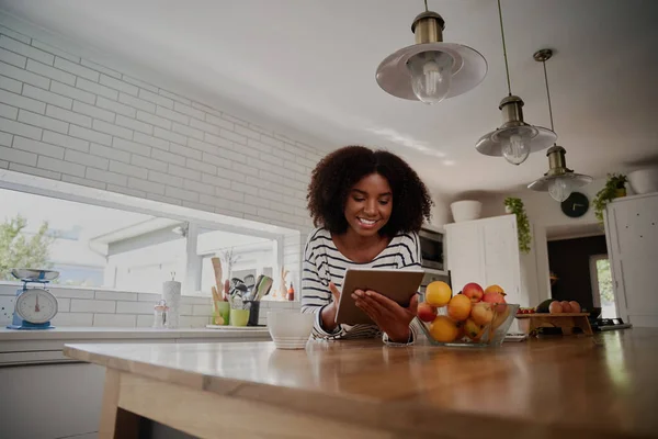 Jovem mulher africana alegre navegando na internet no tablet digital para novas receitas na cozinha moderna — Fotografia de Stock