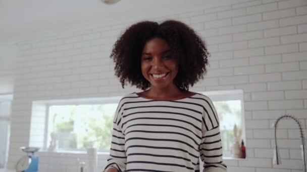 Jovem afro-americana muito sorridente de pé em uma cozinha moderna fritando comida em panela sobre o moderno fogão a gás - alimentação saudável em casa — Vídeo de Stock