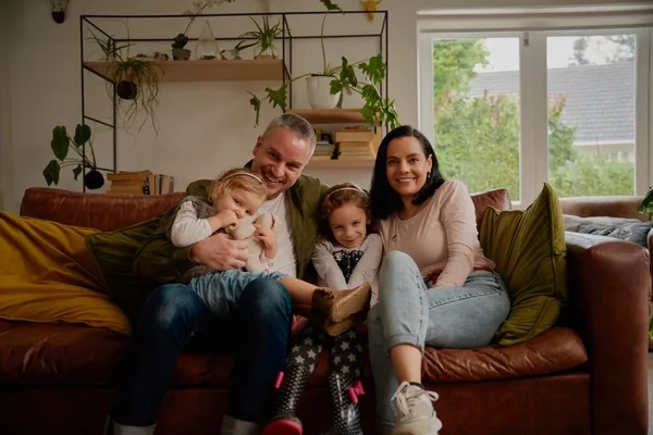 Cheerful couple sitting on couch with two beautiful little daughters at home - one big happy family portrait on a modern couch at home