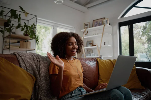 笑顔若いアフリカ系アメリカ人の女性がソファに手を振ってリラックスしながら、自宅でビデオ通話で友人と話をする-若いブロガー家から働く — ストック写真