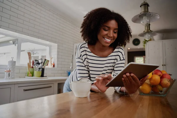 Mulher Africano-Americana em pé na cozinha inclinada no balcão usando tablet digital olhando para receitas on-line — Fotografia de Stock