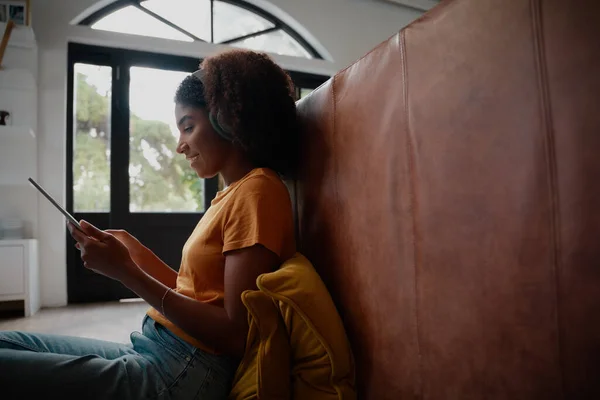 Oldalnézet fiatal afrikai nő ül a padlón a digitális tabletta fülhallgatóval, miközben videohívás — Stock Fotó