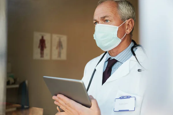 Старший чоловік-лікар стоїть в масці з використанням цифрового планшета в лікарні — стокове фото