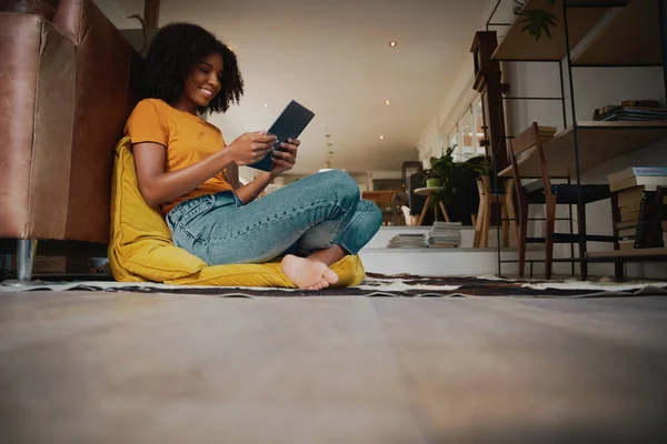Low angle view van de gelukkige Afro-Amerikaanse vrouw met afro zitten op de vloer met een kussen met behulp van een digitale tablet — Stockfoto