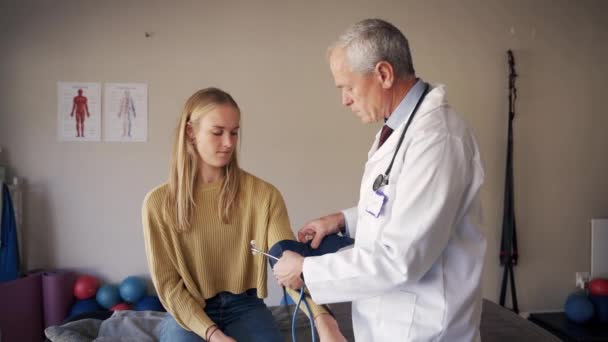 현대 진료소에서 혈압계를 사용하여 혈압 측정을 하고 있는 젊은 여성 환자를 진찰하고 있는 남성 전문의 사 — 비디오