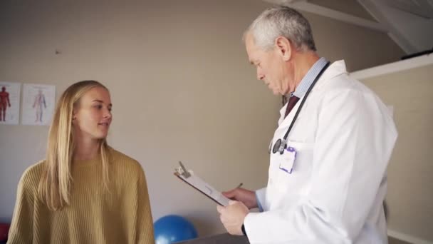 Profissional fisioterapeuta masculino com estetoscópio em torno de seu pescoço examinando jovem mulher pacientes pescoço no consultório da clínica — Vídeo de Stock