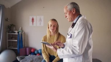 Elinde dijital tablet bulunan kıdemli erkek doktor rehabilitasyon merkezindeki hastaya test sonuçlarını gösteriyor.