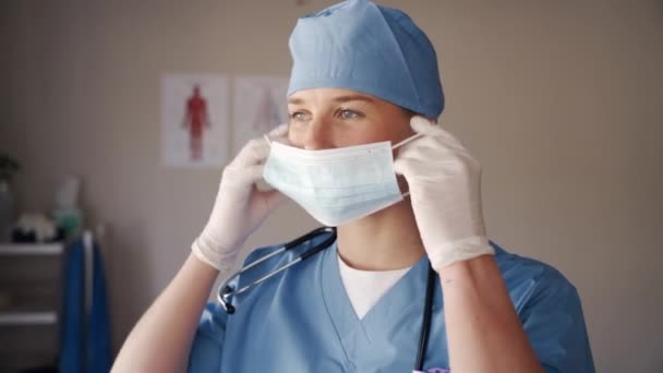 Retrato do jovem profissional médico fisioterapeuta feminino colocando máscara cirúrgica contra o coronavírus — Vídeo de Stock
