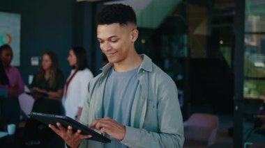 Smiling young businessman using tablet in modern office with colleagues in background