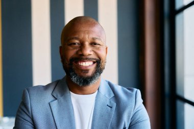 Portrait of smiling African mature businessman in blazer looking at camera in modern office during daytime