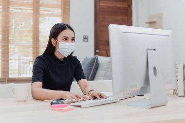 Güzel Asyalı kadın hasta ve evden internet üzerinden çalışmak zorunda. Bir bilgisayar ekranının önünde otururken