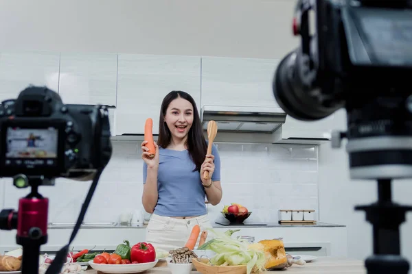 Sosyal medya kavramları. Mutfakta kamerayla bekleyen mutlu bir kadın ve çevrimiçi Mutlu Asyalı kadın vlogger çevrimiçi video yayını. Evde mutfakta yemek pişirmeyi öğretiyor..