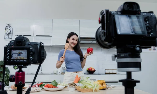 Sosyal medya kavramları. Mutfakta kamerayla bekleyen mutlu bir kadın ve çevrimiçi Mutlu Asyalı kadın vlogger çevrimiçi video yayını. Evde mutfakta yemek pişirmeyi öğretiyor..