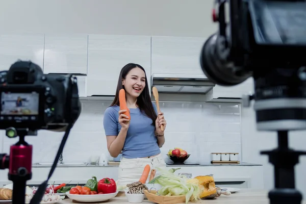 Sosyal medya kavramları. Mutfakta kamerayla bekleyen mutlu bir kadın ve çevrimiçi Mutlu Asyalı kadın vlogger çevrimiçi video yayını. Evde mutfakta yemek pişirmeyi öğretiyor..
