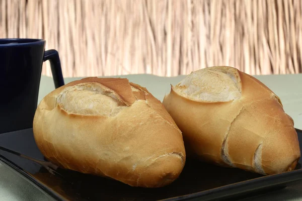 Pão francês, em prato com xícara preta no fundo — Fotografia de Stock