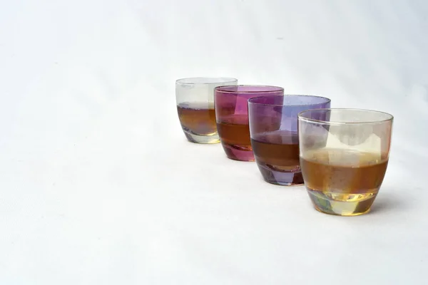 Színes italok üveg csésze asztal, fehér háttér — Stock Fotó