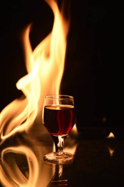 Arkasında ateş olan kırmızı içecek ve siyah arkaplanda yansıma