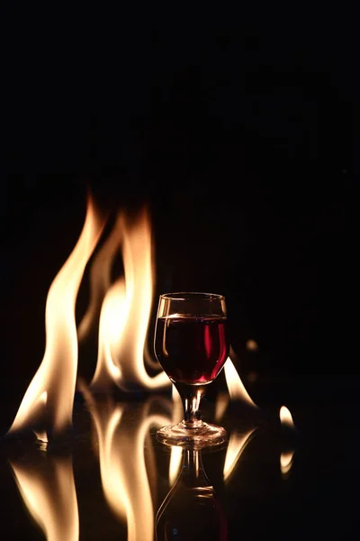 Rood drankje met vuur achter en reflectie op zwarte achtergrond — Stockfoto