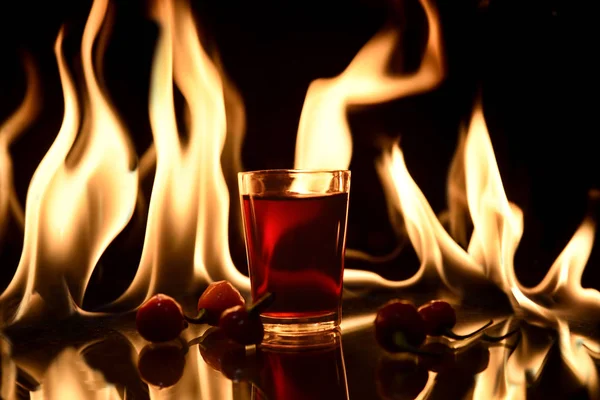 Arkasında ateş olan kırmızı içecek ve siyah arkaplanda yansıma — Stok fotoğraf