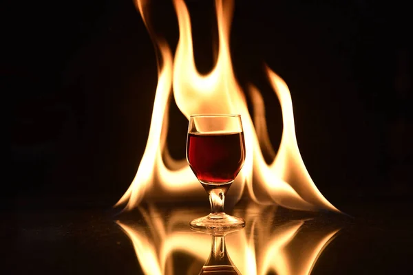 Arkasında ateş olan kırmızı içecek ve siyah arkaplanda yansıma — Stok fotoğraf