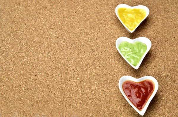 Миска білої форми серця з різнокольоровими соусами на пробці та бамбуку м — стокове фото