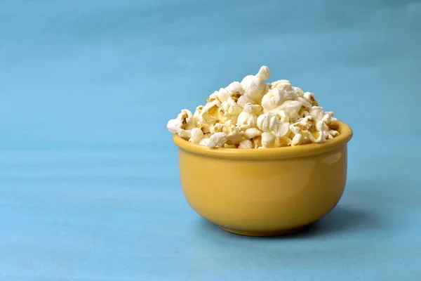 Popcorn in Schale mit rosa Boden mit Mais daneben auf blauem Ba — Stockfoto