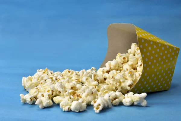 Popcorn fällt aus Papierverpackung mit blauem Hintergrund — Stockfoto