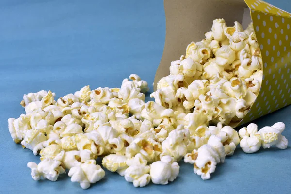 Popcorn fällt aus Papierverpackung mit blauem Hintergrund — Stockfoto
