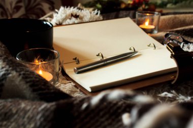 Hygge tarzı. Sıcak battaniye, yanan mumlar, notalar için kitap. vintage tarzı, natürmort.