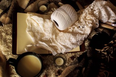 Bir fincan sıcak süt, bir kalem ve bir kitap la rahat bir ev. Hygge tarzı. Sıcak içecek, sıcak battaniye, mum, şiş ve örgü ile bir kupa. vintage tarzı, natürmort.