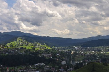 gökyüzünde parlak bulutlar ve güneş ışığı ile güzel bir dağ manzara, kabarık yeşil ladin, ve dağ yamaçlarında konut binaları ile tarifsiz güzellik glade. fantastik açık arka plan.