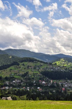 gökyüzünde parlak bulutlar ve güneş ışığı ile güzel bir dağ manzara, kabarık yeşil ladin, ve dağ yamaçlarında konut binaları ile tarifsiz güzellik glade. fantastik açık arka plan.