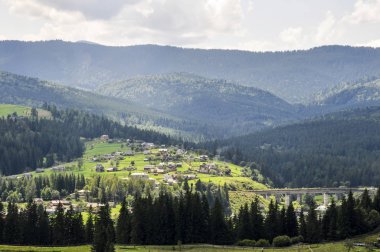 gökyüzünde parlak bulutlar ve güneş ışığı ile güzel bir dağ manzara, kabarık yeşil ladin, ve dağ yamaçlarında konut binaları ile tarifsiz güzellik glade. fantastik açık arka plan.