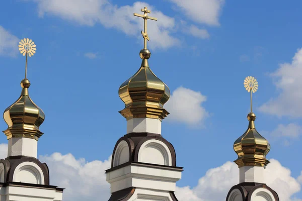 Orthodox crosses on golden domes, three domes on a background of blue sky with clouds