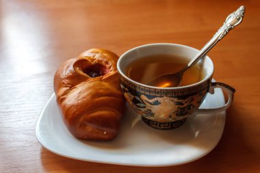 ahşap bir masa üzerinde beyaz bir tabak üzerinde gevrek altın kabuk ve tatlı berry reçel ile lezzetli bir pişmiş çörek ile sıcak çay fincan. soğuk bir sonbahar gününde tatlı atıştırmalık