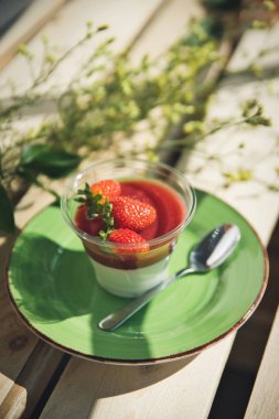 Çiçeklerle ahşap bir arka plan üzerinde bir fincan çilek ile Panacota