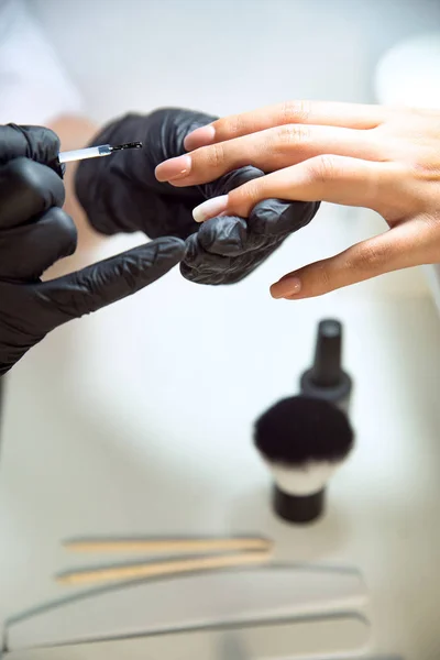 Manicure in guanti neri applica la base sotto uno smalto gel — Foto Stock