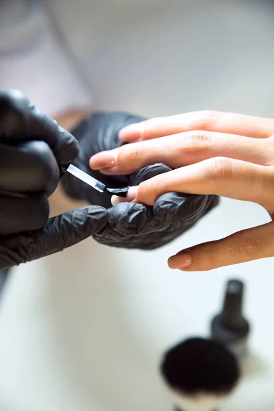 Manicure in guanti neri applica la base sotto uno smalto gel — Foto Stock