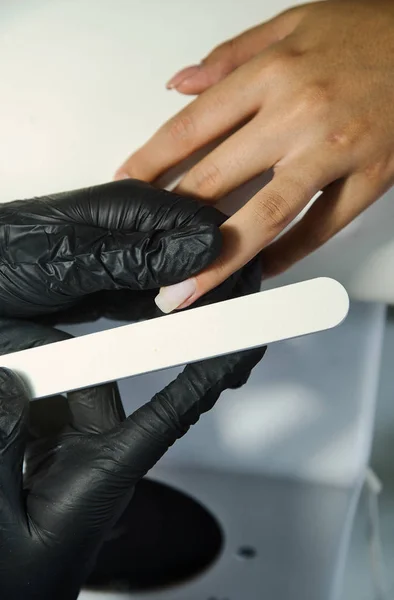 Manicurista al lavoro con una lima per unghie primo piano con guanti neri — Foto Stock