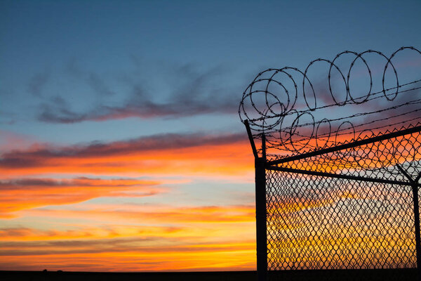 Dramatic sunset with chain link fence and razor wire silhouette.