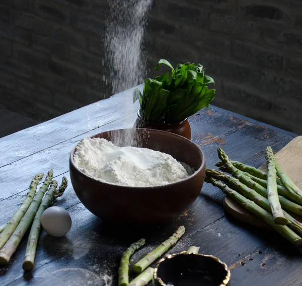 Kase içine un dökülüyor, yeşil kuşkonmaz ve yumurtalı kompozisyon, ev yemeği.