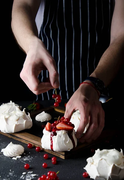Bir adam Pavlova pastasını kırmızı böğürtlenlerle süslüyor.