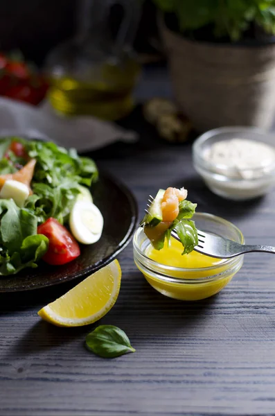 Çatal dolusu salata. Sebze ve somon salatası. Arka planda koyu tabakta, soslarla, koyu ahşap masada dikey yakın plan.