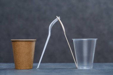 Gri arka planda bambu ahşap ve kağıttan yapılmış çevre dostu tek kullanımlık sofra takımı. Plastik tabak ve çatal bıçak takımı. Çevreye önem vermek. Geri dönüşüm sorunu. Güvenli gezegen, çevre kavramı.