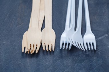 Sıfır atık. Tahta çatal bıçak takımı plastik çatal bıçak takımına karşı. Gri arka planda bambu ahşap ve kağıttan yapılmış çevre dostu tek kullanımlık sofra takımı. Çevreye önem vermek. Geri dönüşüm sorunu.