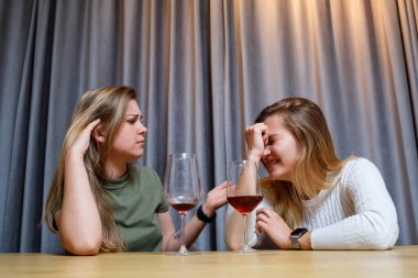 Bir kadın, yardıma ihtiyacı olan üzgün bir arkadaşını teselli eder. Alkol konseptiyle depresyon. Üzgün genç kız elinde bir kadeh şarapla en iyi kız kardeşine bakıyor.