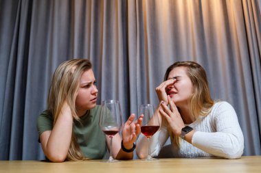 Bir kadın, yardıma ihtiyacı olan üzgün bir arkadaşını teselli eder. Alkol konseptiyle depresyon. Üzgün genç kız elinde bir kadeh şarapla en iyi kız kardeşine bakıyor.