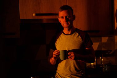 Gün batımında pencerenin önünde duran bir adam mutfakta kahve içiyor.