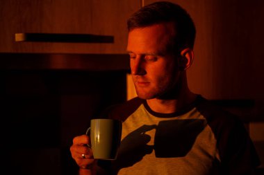 Gün batımında pencerenin önünde duran bir adam mutfakta kahve içiyor.